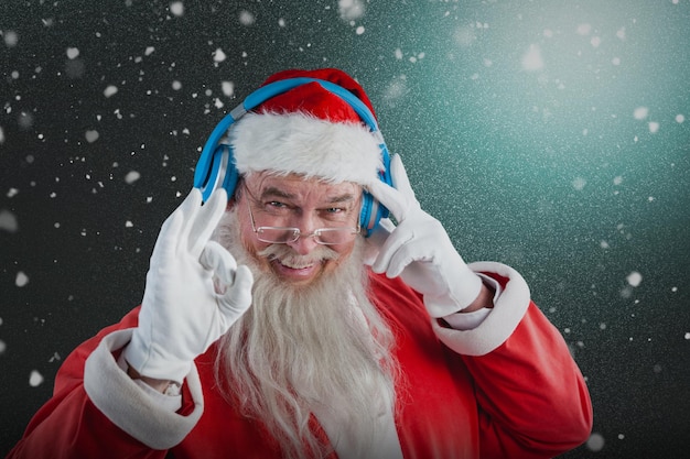 Composite image of portrait of santa claus showing hand okay sign while listening to music on headph