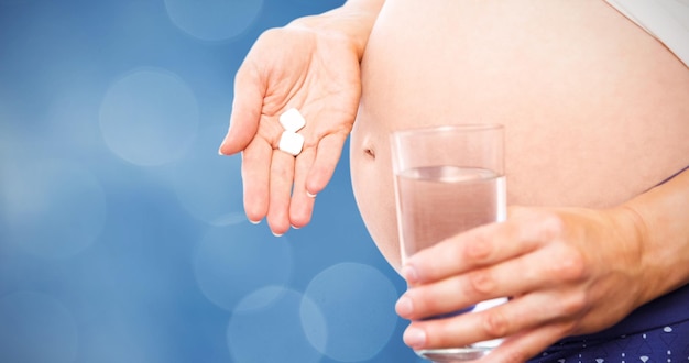 Composite image of pregnant woman taking a vitamin tablet