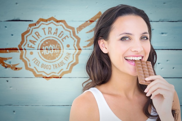 Composite image of pretty brunette eating bar of chocolate