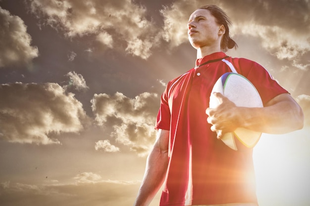 Composite image of rugby player holding football at field