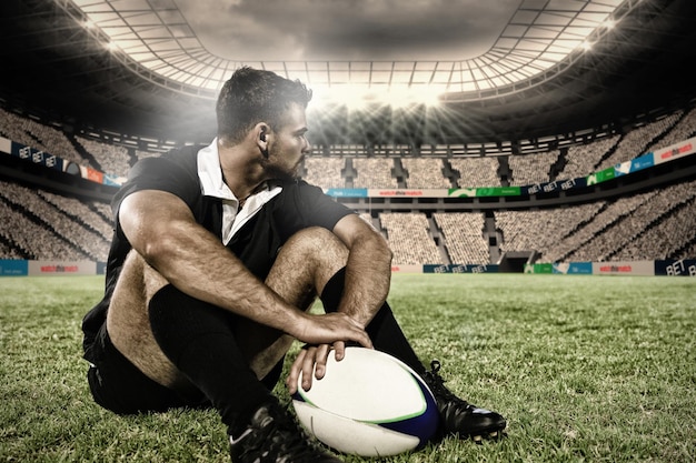 Composite image of rugby player sitting on the field with football