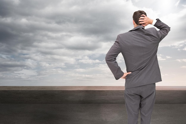 Composite image of young businessman standing back to camera scratching his head