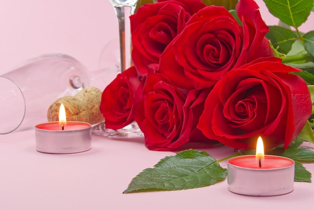 A composition of a beautiful bouquet of roses, candles, glasses and a bottle of champagne creates a romantic card. The concept of st valentine's day, Mother's Day, March 8.