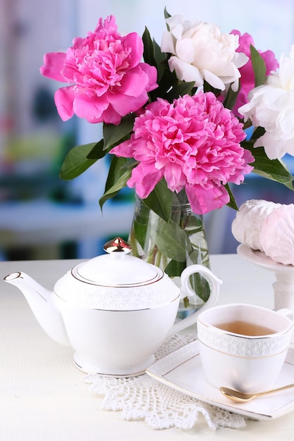 Composition of beautiful peonies in vase, tea in cup and marshmallow, on table, on light background