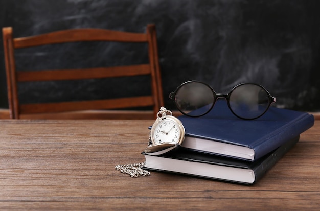 Composition of blue notebooks eyeglasses and vintage clock on wooden table