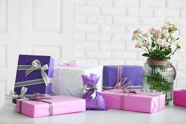 Composition of colourful gift boxes and flowers in glass on white table in front of brick wall background