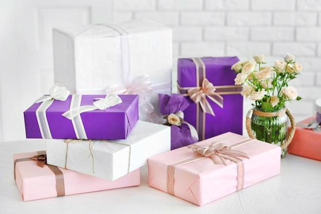 Composition of colourful gift boxes and flowers in glass on white table in front of brick wall background