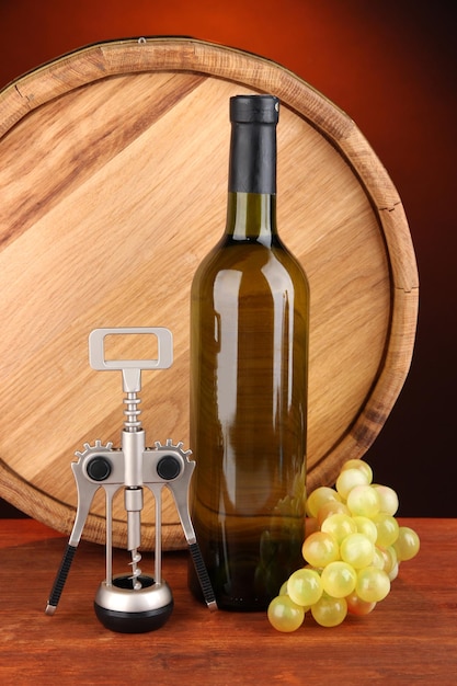 Composition of corkscrew and bottle of wine grape wooden barrel on wooden table on dark background