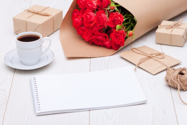 Composition. Cup of coffee, red rosses, gift boxes, notebook. Natural materials concept.