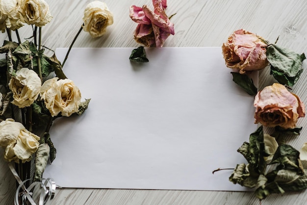 Composition dried rose flowers and sheet of paper for message on a white wooden background Postcard with copy space Frame Place for text design Greeting card Flat lay top view Selective focus