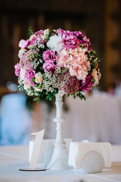 A composition of flowers and green is on a festive table at the wedding banquet hall Stands sign number one Close up