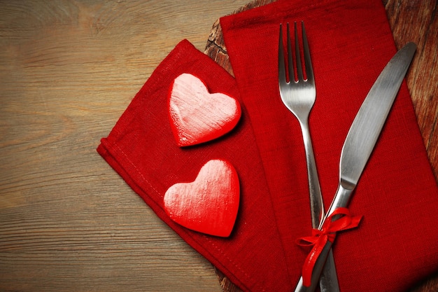 Composition of fork knife napkin and decorative hearts on cutting board on wooden table background