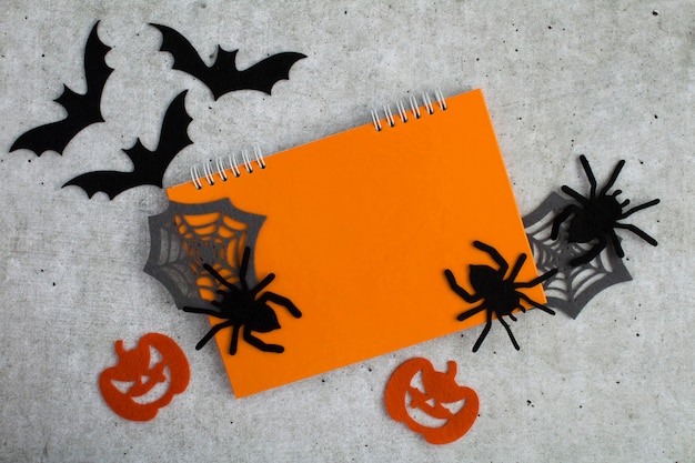 Composition  for Halloween with orange notebook, decorative spiders, pumpkins, spider webs and bats on the gray background. Copy space. Top view.