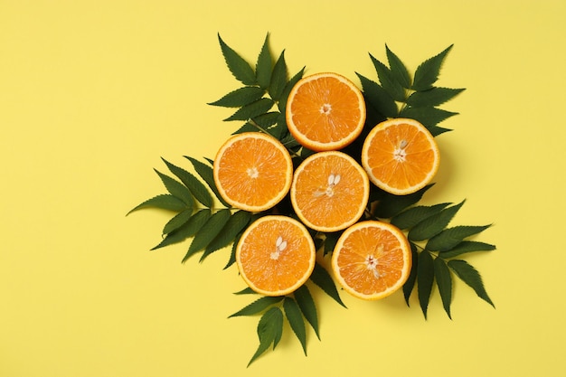 Composition of halves of oranges with green leaves on a bright yellow background Flat lay Copy space