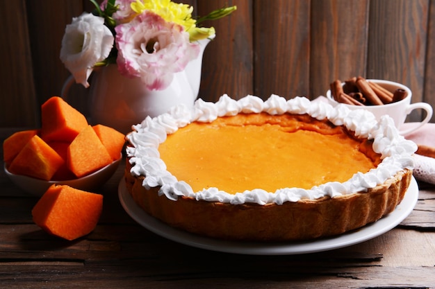 Composition of homemade pumpkin pie on plate and flowers in vase on wooden background