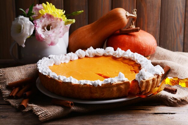 Composition of homemade pumpkin pie on plate and fresh pumpkins on wooden background