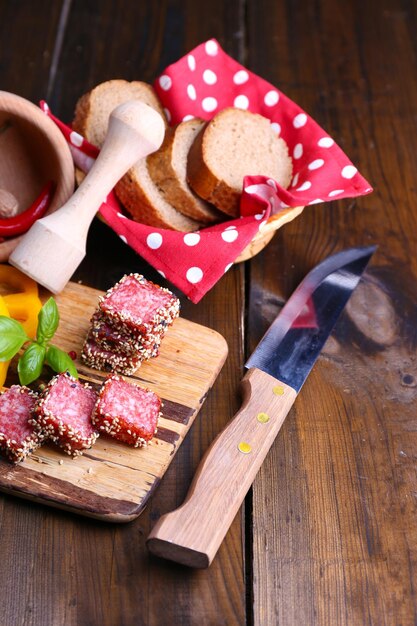 Composition of knife sliced salami sausage with sesame on cutting board on wooden background