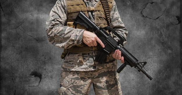 Composition of midsection of soldier holding gun, against smoke on dark background