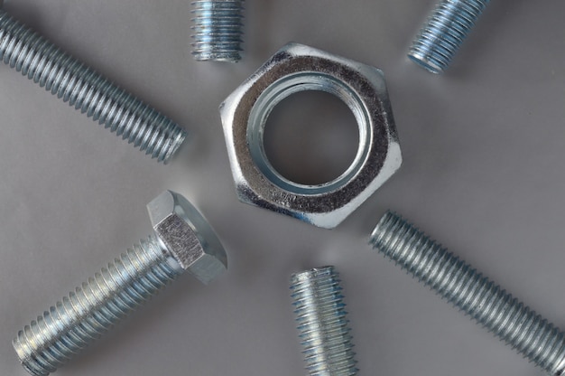 Composition of new bolts and nuts of different sizes on a gray background.