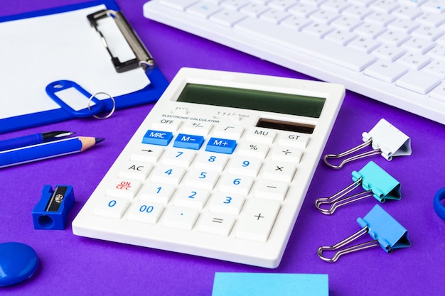 Composition of office lifestyle items on  purple background, computer keyboard office supplies on desk in office