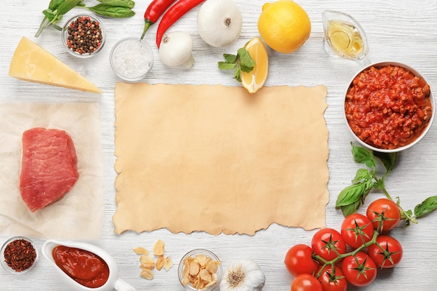 Composition of raw meat with vegetables and paper on wooden background