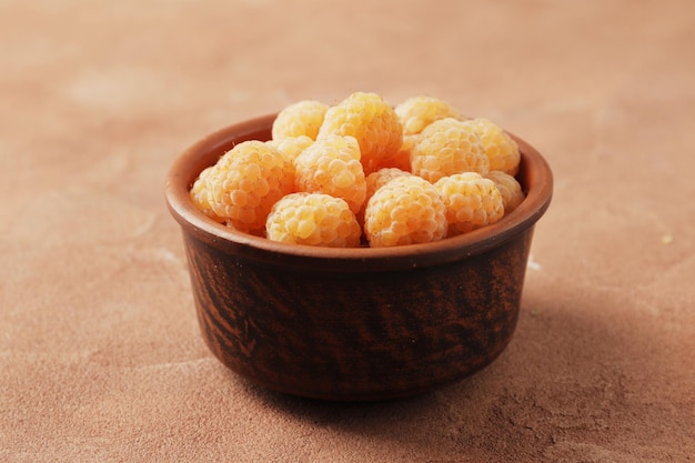 Composition of ripe yellow raspberries in a bowl on a marble background