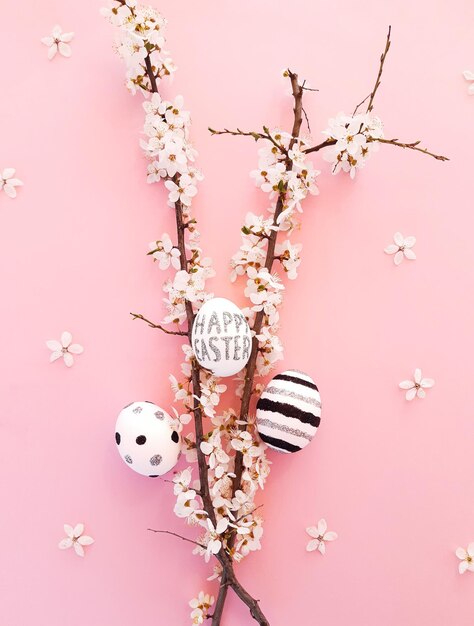 Photo composition of spring flowers, blooming tree branches and eggs with black, silver lines and polka dots on a pink background. glitter inscription happy easter. flat lay, top view, close up, copy space