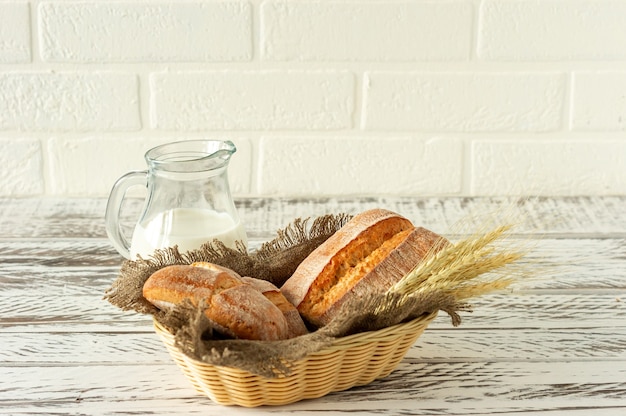 Composition of various baked products in basket on rustic background with jug of milk. Homemade fresh pastry.