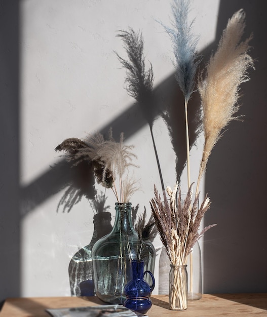 A composition of vases with dried flowers of a different type on a wooden table in light room interi