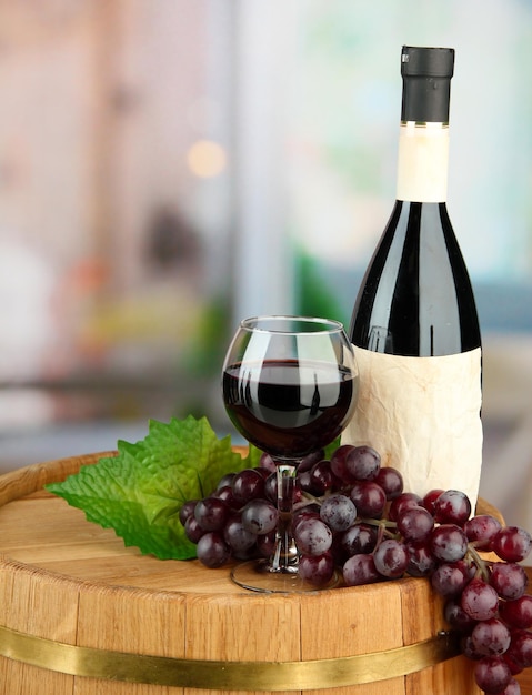 Composition of wine bottle glass and grapeon wooden barrel on bright background