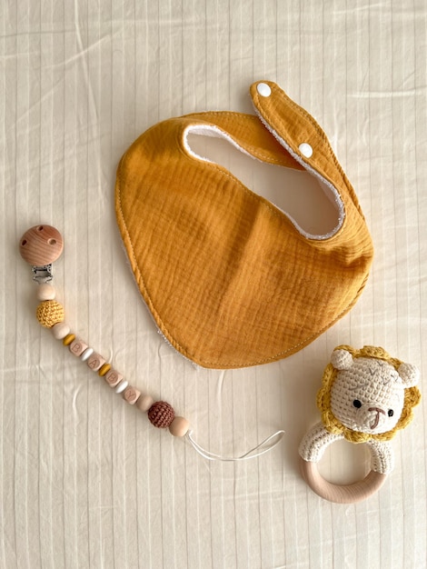 Composition with baby muslin bibs rattles with a knitted bodice and chains of wooden beads with a nipple clothespin on a light background Vertical image