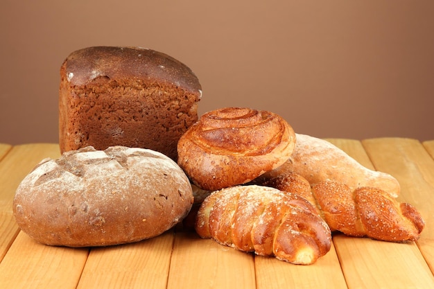 Composition with bread and rolls on wooden table on color background