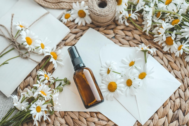 Composition with chamomile flowers and cosmetic bottle of essential oil on white background top view