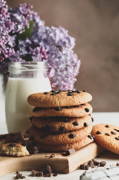 Composition with chocolate chip cookies, milk and lilac on white wooden table