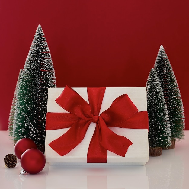 Composition with Christmas gift box with Christmas tree decoration on red background