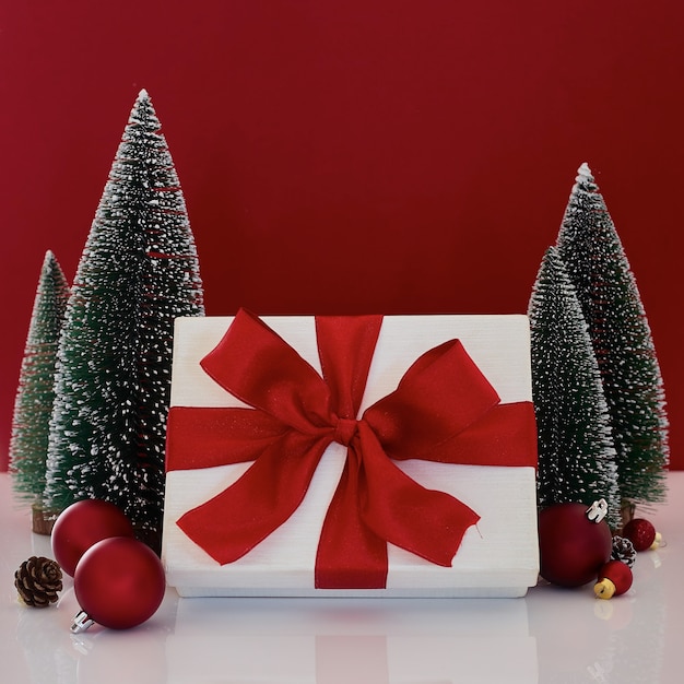 Composition with Christmas gift box with Christmas tree decoration on red background