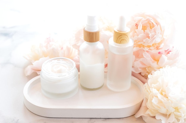 Composition with cosmetic products mockup white jars and bottles and white peonies on a marble background