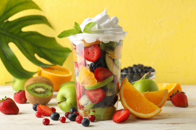 Composition with cup of fresh fruit salad on white wooden table