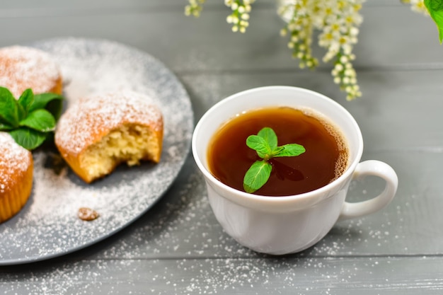 Composition with a cup of tea cupcakes and white cherry flowers on a wooden background