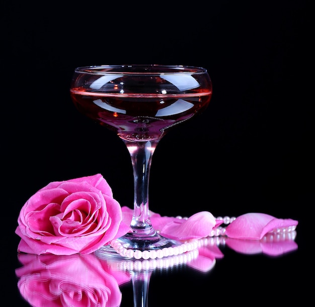 Composition with pink sparkle wine in glass and  rose isolated on black