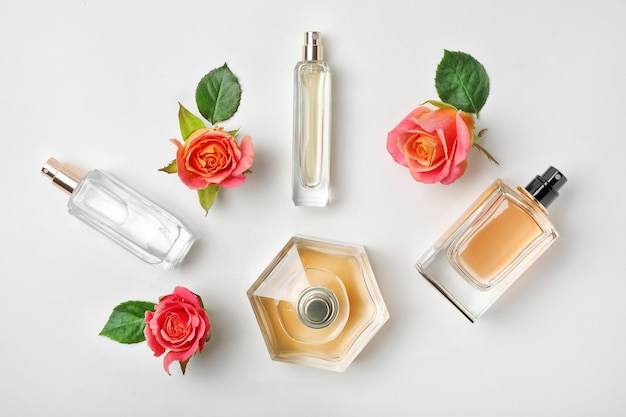 Photo composition with transparent bottles of perfume and beautiful flowers on white background