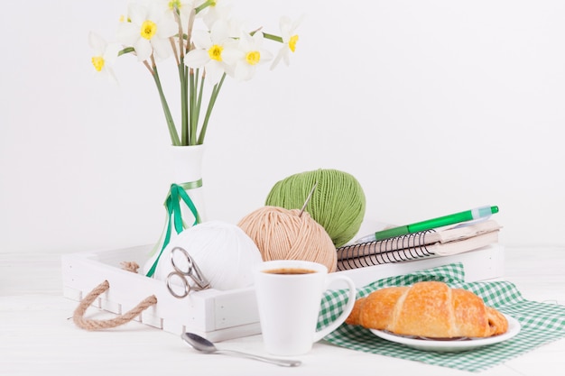 Composition with a vase and a wooden tray and balls of yarn for needlework.