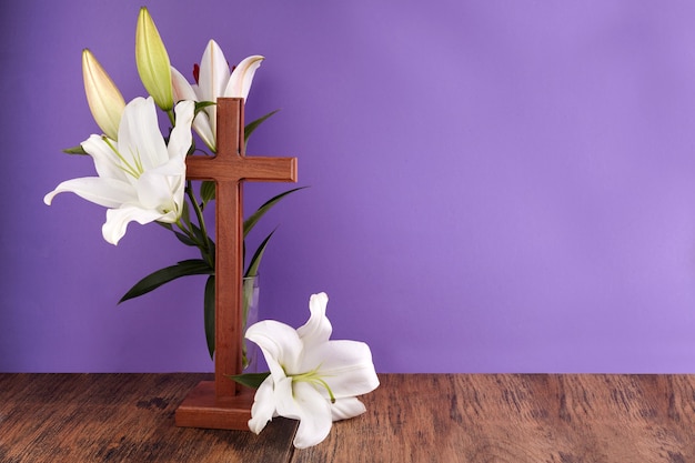 Composition with wooden cross and lily on purple background