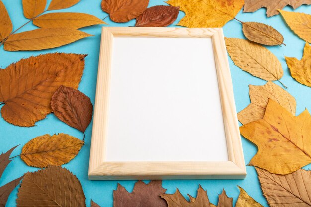 Composition with yellow and brown autumn leaves and wooden frame mockup on blue pastel background side view copy space