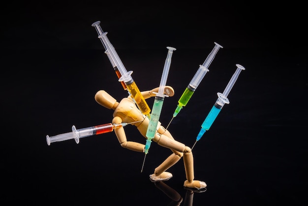 Composition of wooden mannequin with stucked syringes on black background drug addiction concept