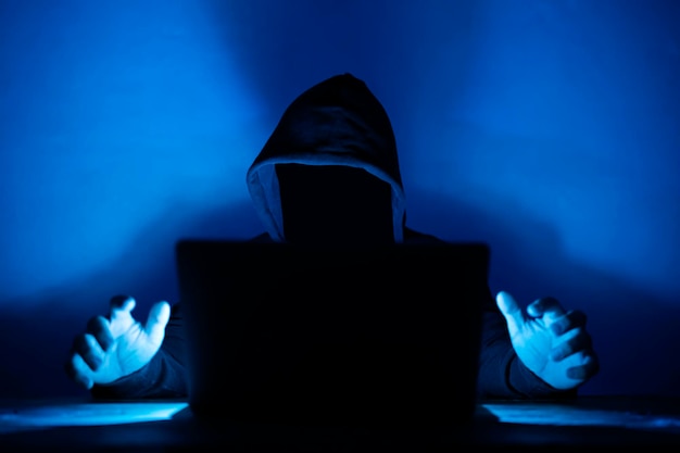 Computer hacker with hoodie and obscured face Hacker in front of his computer Dark face