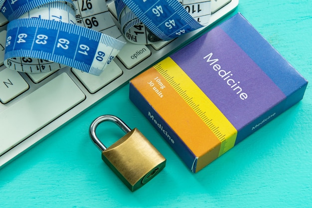 Photo computer keyboard with tape measure and medicine box next to a closed padlock