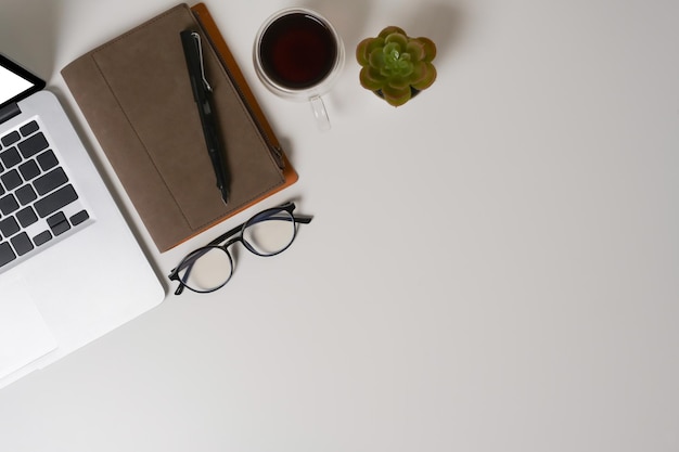 Computer laptop coffee cup and notebook on white table