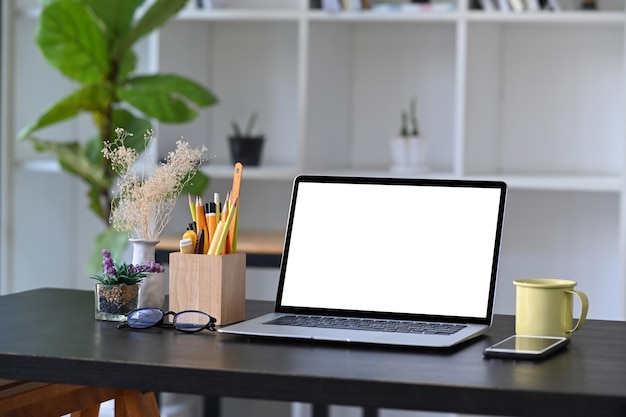 Computer laptop coffee cup and pencil holder on wooden table in home office