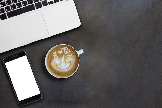 Computer laptop and mobile phone and art latte on black wooden table